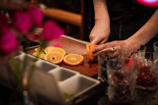 A selective focus shot of the bartender slicing orange on a trey